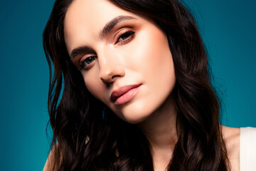 Fototapeta premium Portrait of a confident brunette woman with flawless makeup and wavy hair posing against a blue gradient background