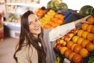 Happy young brunette woman buying fresh grapefruits while grocery shopping in a supermarket, selecting healthy food for her family. Woman straight hand to fruit.