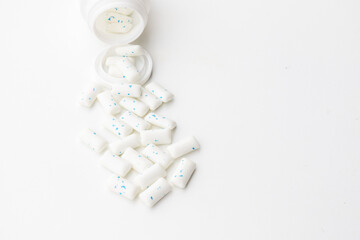An aesthetically arranged shot of white candy pills spilling onto a white background, creating a soft, clinical, and pure visual.