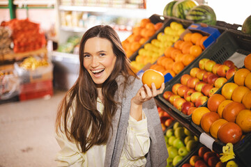 Happy young brunette woman buying fresh grapefruits while grocery shopping in a supermarket, selecting healthy food for her family. Woman hold fruit.