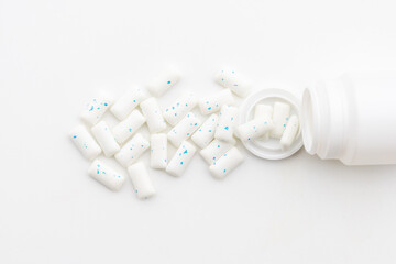 A neat composition of white candy pills placed near an open white bottle, offering a sleek and neutral healthcare-related design.