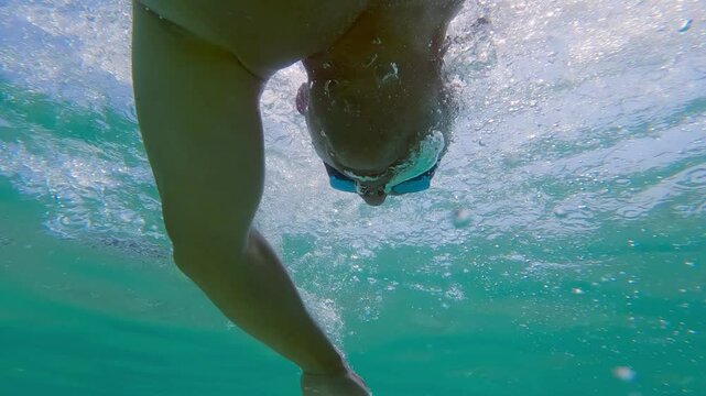 Professional man swimming crowl freestyle in clear blue ocean water on a sunny day, underwater slow motion view