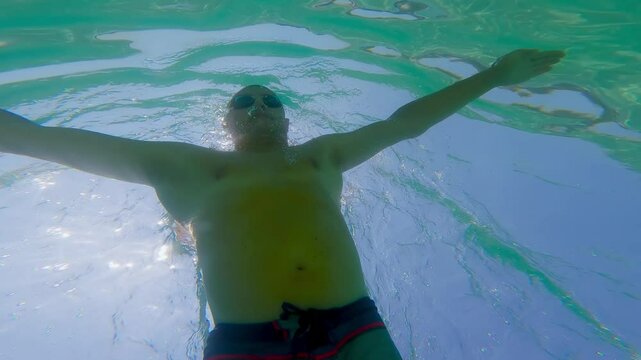 Underwater view of fit man wearing goggles swimming breaststroke underwater in the crystal-clear sea