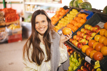 Happy young brunette woman buying fresh grapefruits while grocery shopping in a supermarket, selecting healthy food for her family. Woman hold fruit.