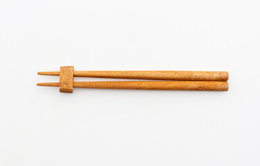 A pair of wooden chopsticks resting on their holder against a clean white background, highlighting simplicity and elegance.