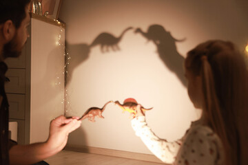 Father and his daughter performing shadow play with toy dinosaurs at home, closeup