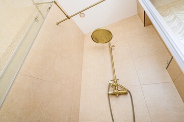 Elegant bathroom interior featuring a golden shower fixture with beige tile backdrop.