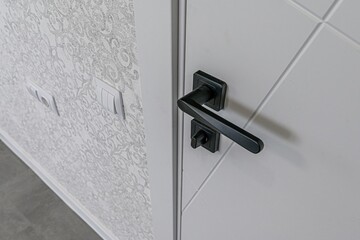 close-up shows a white door with a modern black handle. The adjacent wall has patterned wallpaper...