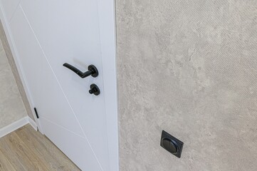 Close-up of a white door with a black handle, adjacent to a textured wall with electrical outlets and a white nightstand.