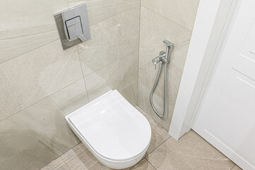 clean, modern bathroom featuring a wall-mounted toilet, bidet sprayer, and tiled walls. The color...