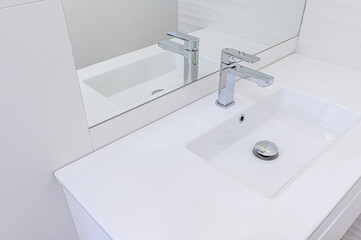 modern, minimalist bathroom sink with a chrome faucet and a mirror reflecting the setup. The clean white aesthetic gives a sense of sophistication.