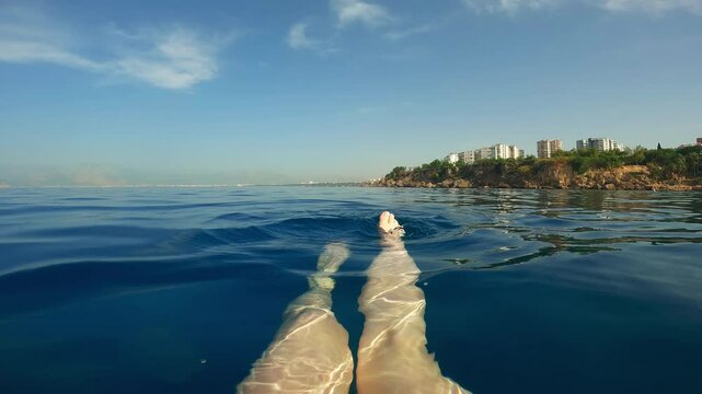 First person view, woman swimming in water and dangling her legs in the sea.