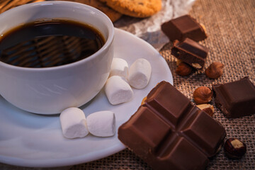 Close-up of coffee, chocolate, marshmallows, and cookies on burlap