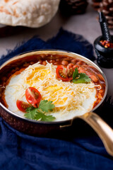 Baked Eggs with Baked Beans, Cheese and Tomato cooked in a frying pan on table side view of breakfast or brunch dish