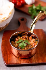 Foul Garnished with cilantro, with bread, tomatoes, and garlic served in a copper pot on a wooden board side view of an Egyptian bean stew