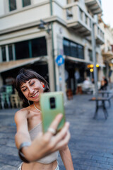 Fototapeta premium Young woman walks the streets and takes selfie using smartphone camera. Beautiful young photographer takes pictures for her travel blog.