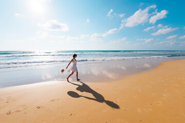 happy girl in a white dress runs along the beach and enjoys her vacation. A carefree girl walks along the beach on a sunny day.