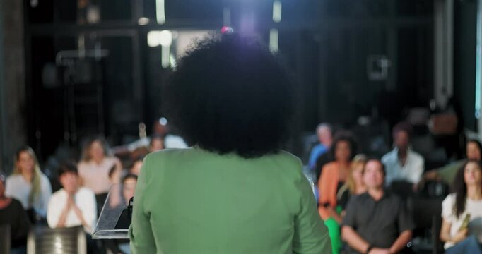 Back view of a woman delivering a speech to an engaged audience, inspiring spiritual gathering, diverse crowd listening attentively to community leader