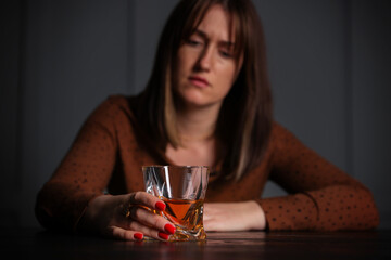 Alcohol addiction. Woman with glass of whiskey at wooden table indoors, selective focus
