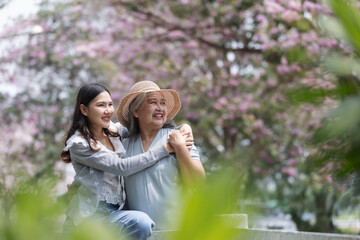Naklejka premium A loving daughter embraces her mother, both smiling under blooming cherry blossoms. 