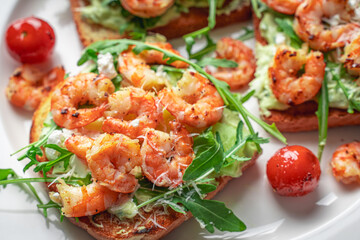 Toast with shrimp, avocado and arugula on a white plate with cherry tomatoes. Close-up. Healthy and...