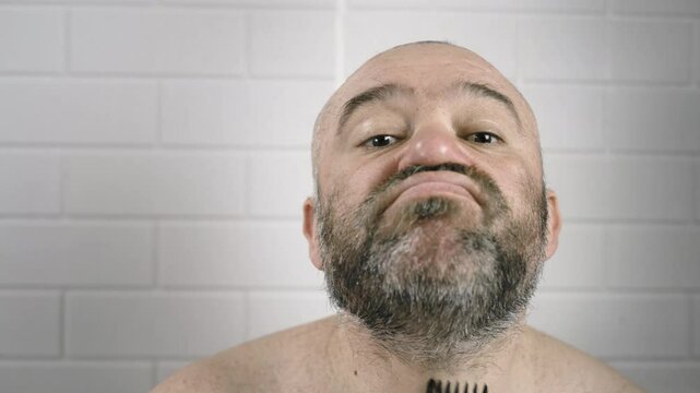 Bearded man cutting his beard with clippers in front of mirror in bathroom at home