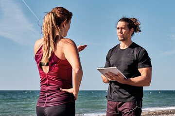 Personal trainer taking notes while listening to client on beach