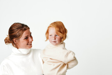 Mother and daughter embracing in cozy white sweaters on bright background for family, love, and parenthood concept