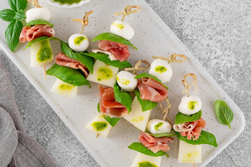 Appetizer with melon, mozzarella, prosciutto ham and fresh basil on stick with pesto sauce on a...