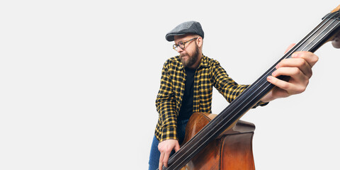 Close-up of man, musician in plaid shirt and cap playing double bass, deeply engaged in rhythm,...