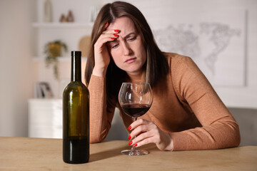 Alcohol addiction. Miserable woman with wine at table indoors