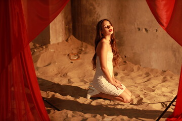 Pretty young brunette woman in white dress sitting in the sand