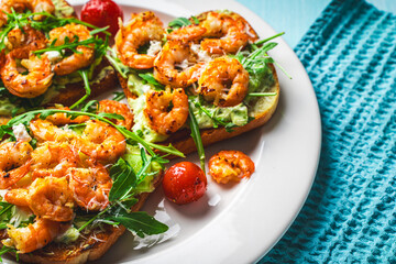 Toast or sandwiches with avocado oil, arugula and fried prawns on a white plate on a light blue background with a napkin. Healthy breakfast. View from above. Flat layout. Space for text.