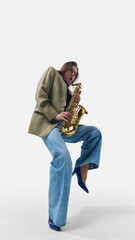 Stylish young woman in vintage blazer and wide-leg jeans, lifting leg while passionately playing...