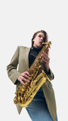 Fototapeta premium Low-angle image of woman in blazer, fingers pressing golden saxophone keys, fully immersed in rhythm, playing on white background. Concept of music, jazz, festival, performance, artistic life, energy