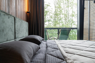 Fototapeta premium design of modern bedroom in country house or villa. bedroom has brown wooden walls and large windows. Large double bed with upholstered headboard, clean linen and bedspread. wooden table near bed