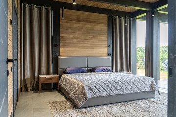 design of modern bedroom in country house or villa. bedroom has brown wooden walls and large windows. Large double bed with upholstered headboard, clean linen and bedspread. wooden table near bed