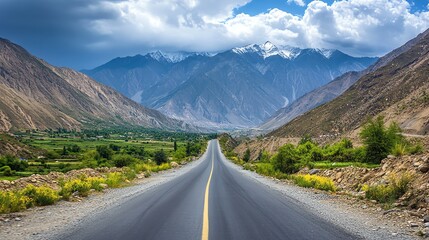 Fototapeta premium Driving Asphalt Road Through Valley with Snowy Mountains and Cloudy Sky