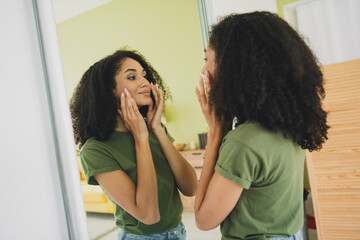Photo of pretty young girl touch face look mirror wear t-shirt weekend pastime apartment indoors