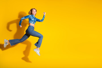 Fototapeta na wymiar Young woman in stylish outfit joyfully jumping against a vibrant yellow background providing a cheerful and energizing atmosphere