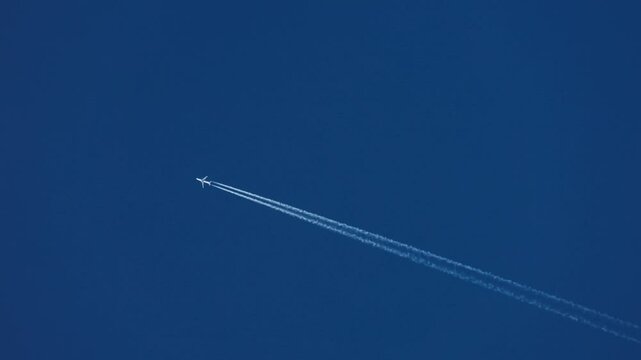 The journey begins, plane flies high in the blue sky, leaving a white trail. Jet airplane flying overhead in clear blue sky and leaving nice contrail. Plane smoothly as it flies through the sky