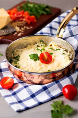 Cheesy Baked Eggs garnished with cheese, tomato and parsley served in a copper pan isolated on napkin side view of Middle Eastern breakfast dish