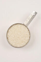 A top-down view of a stainless steel measuring cup filled to the brim with white sushi rice against a plain background