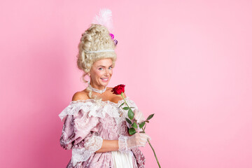 Elegant woman in baroque costume holding a rose against a pastel pink background