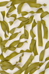 A flat-lay shot of numerous spinach-infused wide tagliatelle pasta pieces scattered randomly on a...