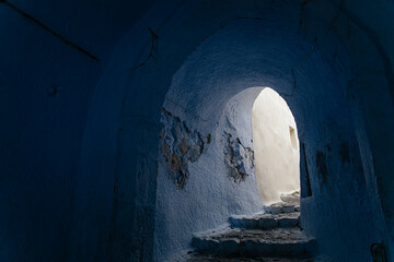 Rustic stone staircase in a whitewashed tunnel, Pyrgos Kallistis, Santorini, Greece. Traditional Cycladic architecture with aged walls and light contrast in a charming Greek island alleyway.