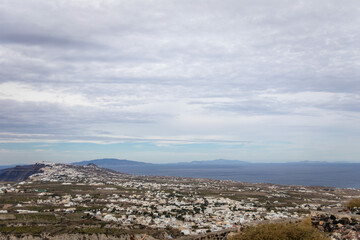 Horizontal view from Pyrgos Kallistis Castle, showcasing panoramic vistas of north Santorini, the Aegean Sea, Greek islands, and coast, with a cruise ship, cloudy sky, and Fira in the distance
