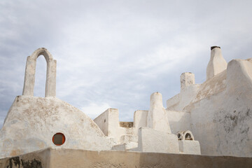 Horizontal photo of white-washed Greek traditional beautiful old house with tower, chimney and cloudy sky in Pyrgos Kallistis, Santorini, Greece - a hidden gem to explore in the Greek islands mainland