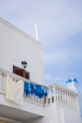 White washed traditional house in Pyrgos Kallistis in Santorini island, Greece, with blue laundry towels in greek colours drying on the clothesline outside of a window on a balcony with cloudy sky