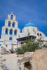 Vertical view of white Greek orthodox church dome and tower and bells with cross in Pyrgos Kallistis, Santorini, Greece with bright blue sky. A perfect day trip destination from Fira.